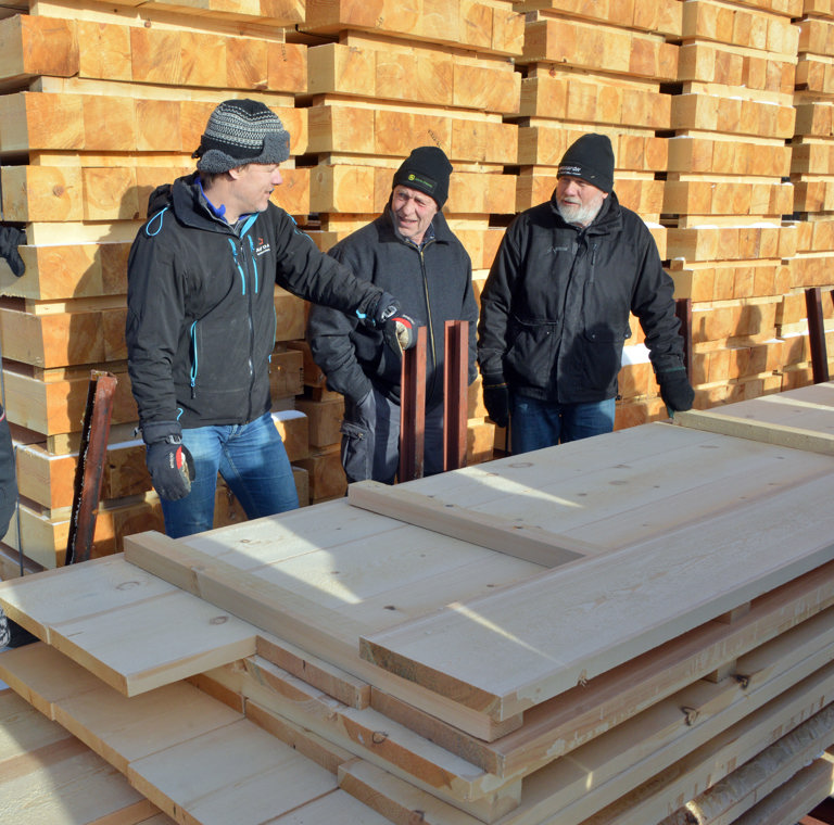 Gigantisk fra fjellskogen. Jakob Trøan ved Materialbanken (t.v.) forteller om store dimensjoner på plank og tømmer i materialbanken til Bjørn Flittie fra Lesja og Hans Hagen fra Sjåk. Foto: Bård Bårdløkken
